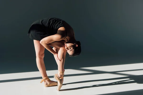 Joven bailarina en vestido negro estirándose a la luz del sol - foto de stock