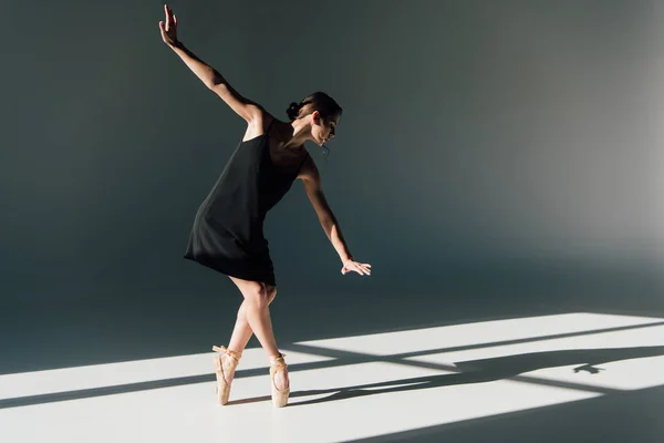 Elegante joven bailarina en vestido negro bailando a la luz del sol - foto de stock