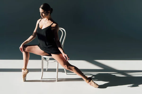 Atraente jovem bailarina em vestido preto alongamento na cadeira branca — Fotografia de Stock