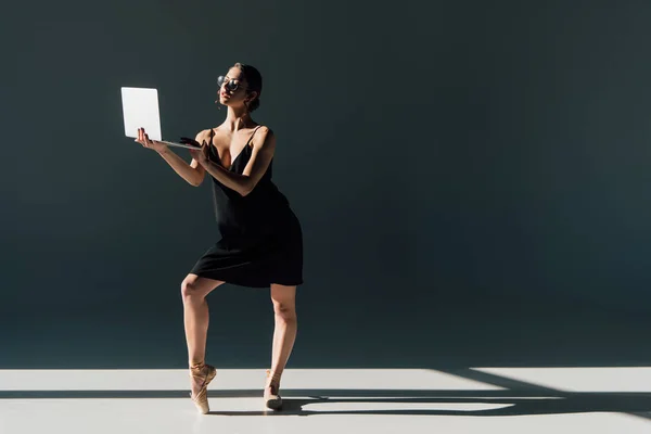 Schöne Ballerina in schwarzem Kleid und Brille posiert mit Laptop — Stockfoto