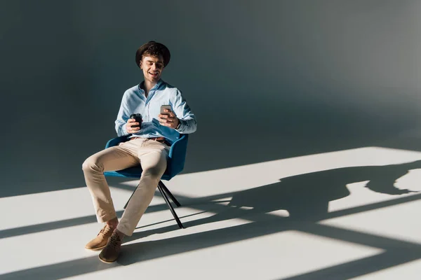 Улыбающийся мужчина использует смартфон, сидя на стуле — стоковое фото
