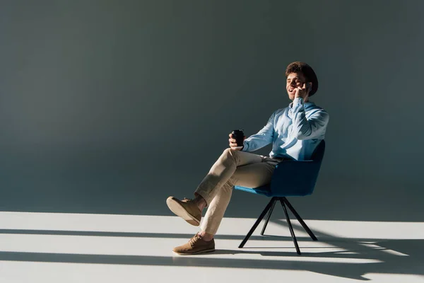 Sorrindo homem falando no smartphone enquanto sentado na cadeira à luz do sol — Fotografia de Stock