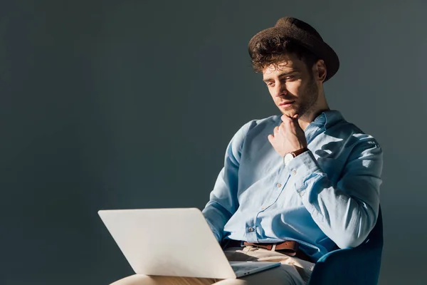 Вдумливий чоловік використовує ноутбук, сидячи на сонячному світлі — стокове фото