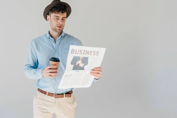 Homem bonito lendo jornal de negócios e segurando copo de papel isolado em cinza — Fotografia de Stock