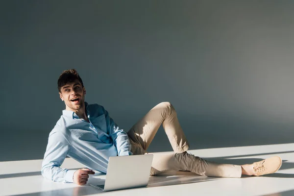 Hombre guapo alegre usando el ordenador portátil mientras está sentado en la luz del sol - foto de stock
