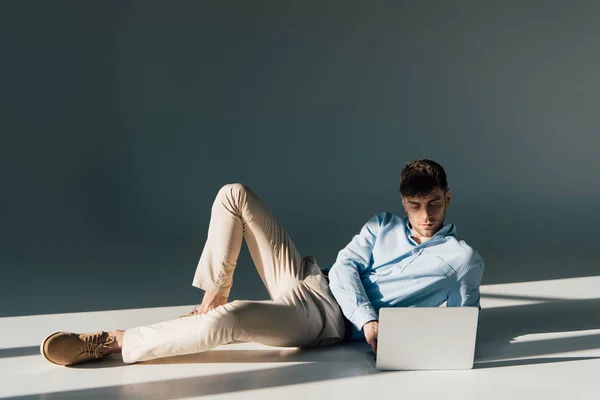 Homem bonito usando laptop enquanto deitado à luz do sol — Fotografia de Stock