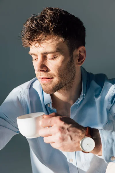 Bonito homem pensativo segurando xícara de café enquanto sentado à luz do sol — Fotografia de Stock