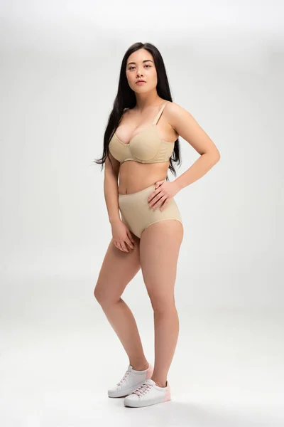 Schöne brünette Mädchen mit der Hand auf der Hüfte, die in die Kamera schaut, isoliert auf grau, Body Positivity Konzept — Stockfoto