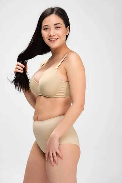 Smiling woman in underwear touching hair and looking at camera isolated on grey, body positivity concept — Stock Photo