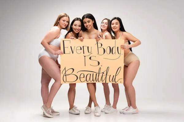 Five pretty young multiethnic women in underwear and sneakers holding placard with 