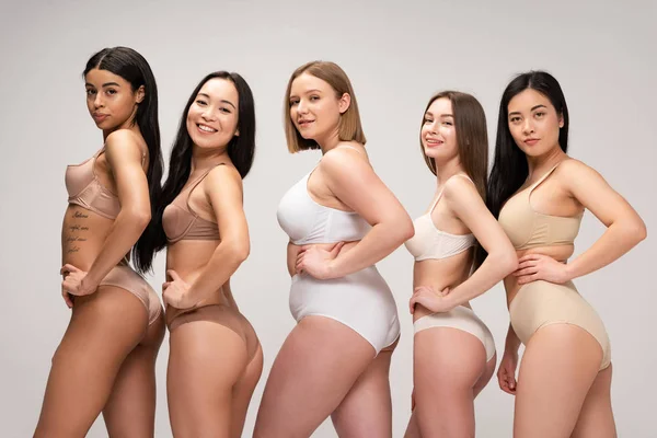 Cinco chicas muy multiétnicas en lencería posando en la cámara con las manos en las caderas aisladas en gris, concepto de positividad corporal - foto de stock