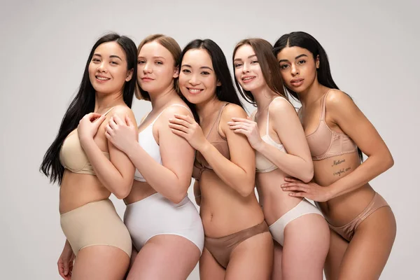 Cinque giovani donne felici che si abbracciano e sorridono isolate sul grigio, concetto di positività del corpo — Foto stock