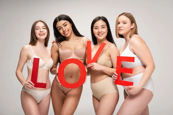 Four beautiful multiethnic girls in underwear holding paper cut word 