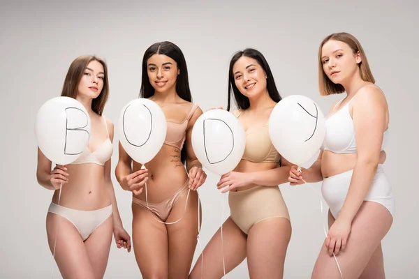 Cuatro atractivas mujeres multiétnicas en lencería sosteniendo globos aéreos con letras 