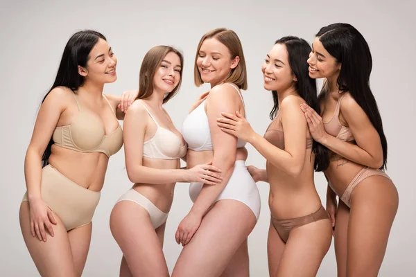 Пять мультиэтнических жизнерадостных молодых женщин, улыбающихся и позирующих перед камерой, изолированных на сером, концепция позитивности тела — стоковое фото