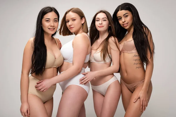Four beautiful multicultural girls smiling and looking at camera isolated on grey, body positivity concept — Stock Photo