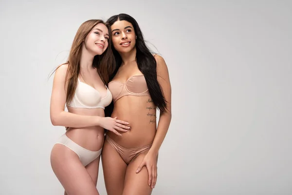 Zwei hübsche multikulturelle Mädchen, die aufblicken, während sie isoliert auf grau vor der Kamera posieren — Stockfoto