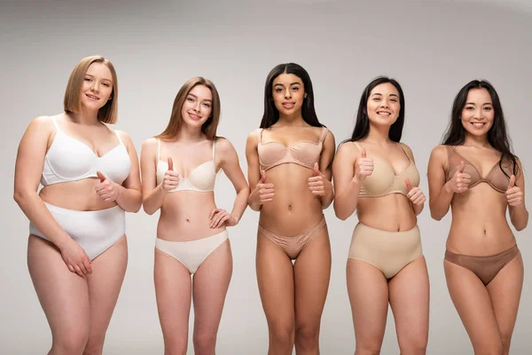 Пять довольно мультикультурных девушек в нижнем белье показывая большие пальцы вверх изолированы на сером, концепция позитивности тела — стоковое фото