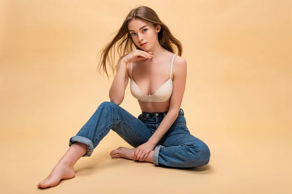 Menina bonita pensativo em jeans azul e sutiã sentado e segurando a mão perto do rosto — Fotografia de Stock