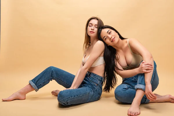 Dreamy young women sitting in blue jeans and bras, body positivity concept — Stock Photo