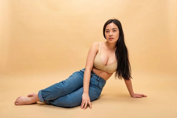 Pretty girl in blue jeans and bra sitting and looking at camera, body positivity concept — Stock Photo