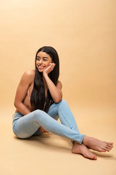 Happy african american girl in blue jeans and bra sitting and looking away — Stock Photo