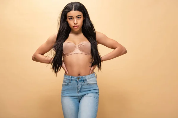 Attrayant afro-américain fille en jeans bleus et soutien-gorge tenant la main sur les hanches et regardant la caméra — Photo de stock