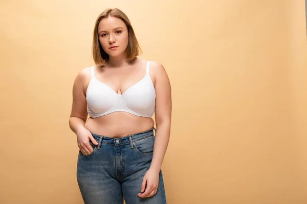 Pensive overweight girl looking at camera while holding hand in pocket isolated on beige, body positivity concept — Stock Photo