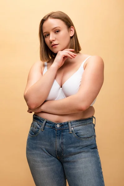 Pensive overweight girl looking at camera while holding hand near face isolated on beige, body positivity concept — Stock Photo