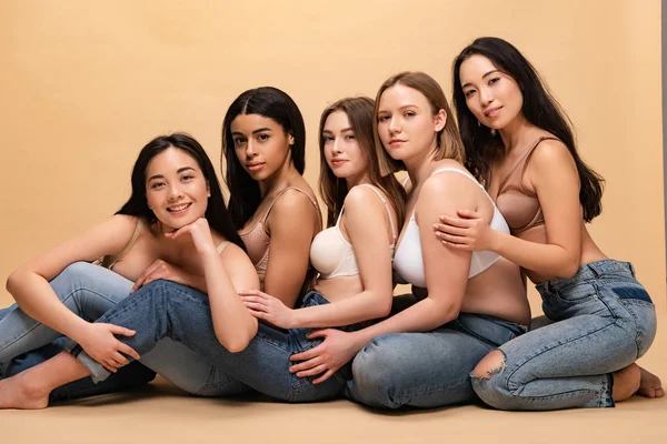 Cinco mulheres multiculturais sorridentes sentadas juntas e olhando para a câmera, conceito de positividade corporal — Fotografia de Stock