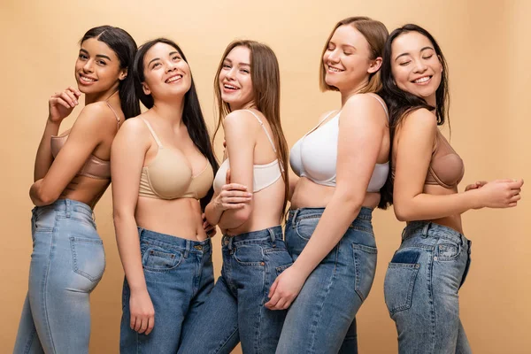 Cinco alegres mujeres multiculturales sonriendo y posando a cámara aislada en beige, concepto de positividad corporal - foto de stock