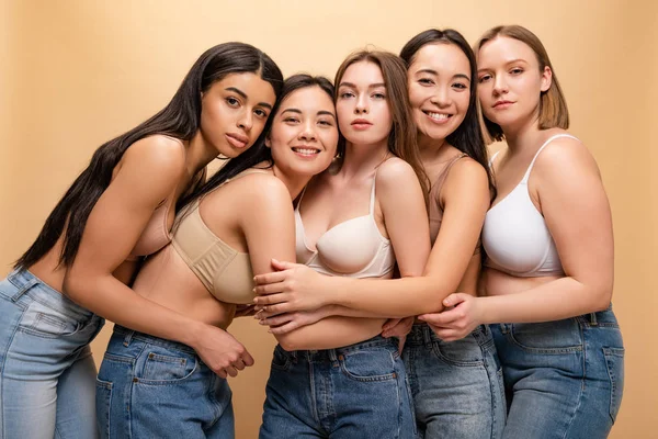 Cinco hermosas chicas multiculturales apoyadas una en la otra y mirando a la cámara aislada en beige, concepto de positividad corporal - foto de stock