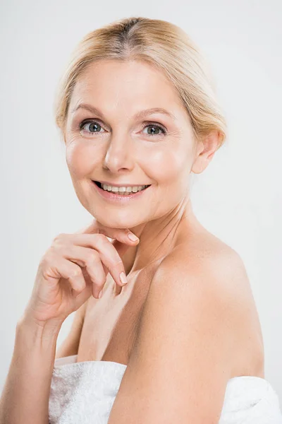 Schöne und lächelnde reife Frau, die in die Kamera schaut und ihr Gesicht auf grauem Hintergrund berührt — Stockfoto