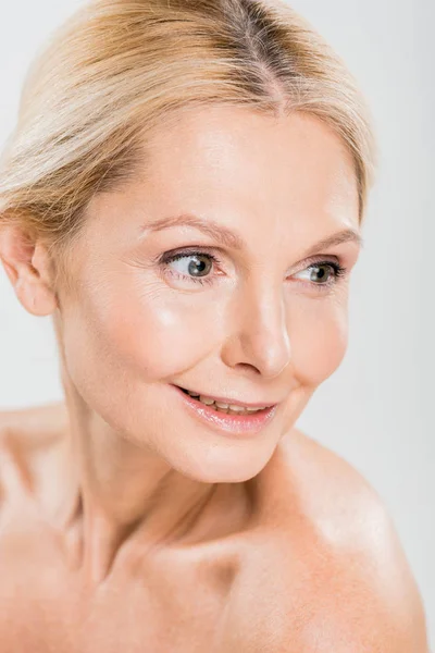 Attraktive und lächelnde reife Frau, die auf grauem Hintergrund wegschaut — Stockfoto