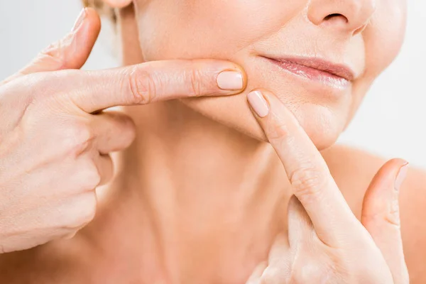 Partial view of mature woman pushing blackheads on her face with fingers on grey background — Stock Photo