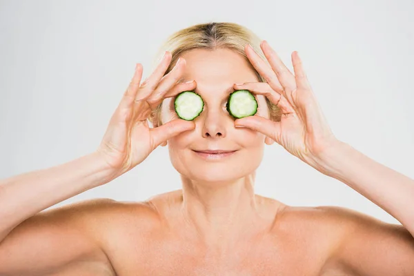 Hermosa y rubia madura mujer sosteniendo corte pepino sobre fondo gris - foto de stock