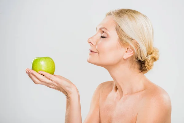 Seitenansicht der schönen reifen Frau mit geschlossenen Augen hält reifen Apfel auf grauem Hintergrund — Stockfoto