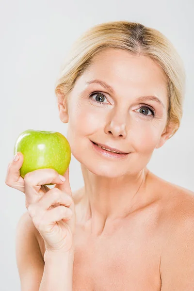 Schöne reife Frau mit grünem Apfel und Blick in die Kamera auf grauem Hintergrund — Stockfoto