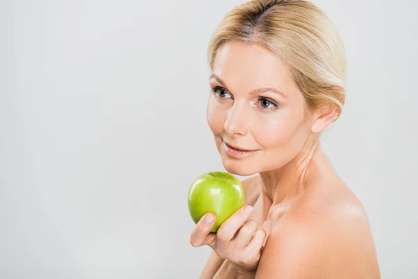 Красива і зріла жінка тримає зелене яблуко і дивиться ізольовано на сірому — стокове фото