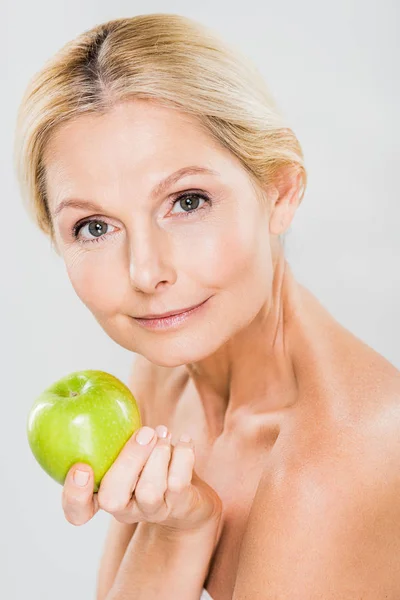 Красива і зріла жінка тримає зелене яблуко і дивиться на камеру ізольовано на сірому — стокове фото