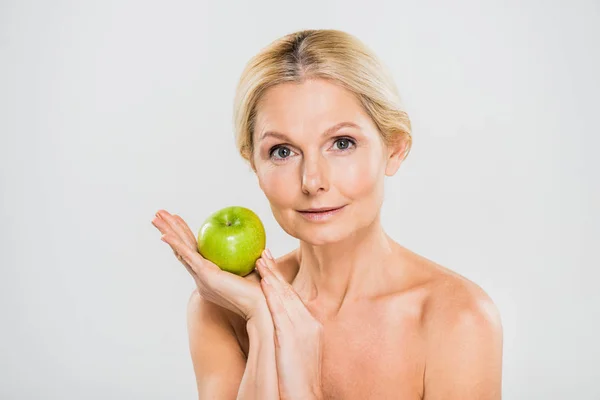 Beautiful and mature woman holding green ripe apple and looking at camera isolated on grey — Stock Photo