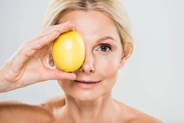 Красива і зріла жінка тримає стиглий лимон і дивиться на камеру ізольовано на сірому — стокове фото