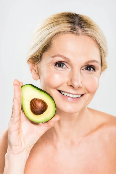 Hermosa y sonriente mujer sosteniendo aguacate y mirando a la cámara aislada en gris - foto de stock