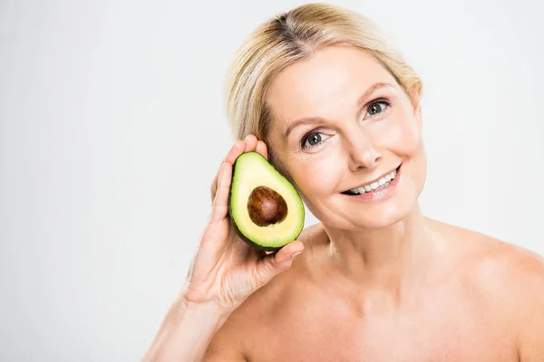 Beautiful and smiling woman holding avocado and looking at camera on grey background — Stock Photo