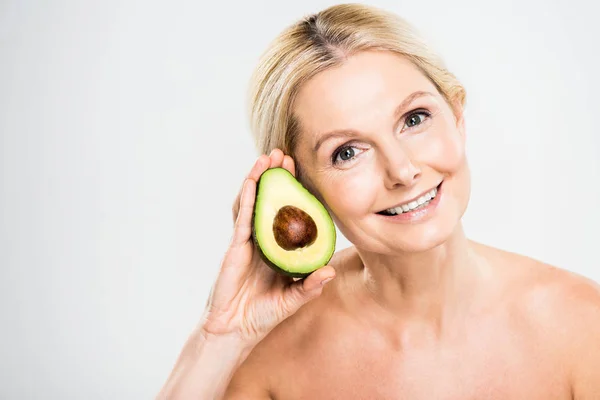 Schöne und lächelnde Frau mit Avocado und Blick in die Kamera auf grauem Hintergrund — Stockfoto