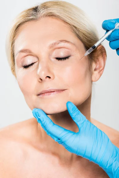 Beautiful and mature woman with closed eyes getting beauty injection isolated on grey — Stock Photo