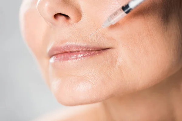 Selective focus of beautiful and mature woman with closed eyes getting beauty injection isolated on grey — Stock Photo