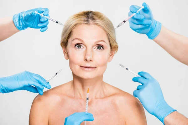 Beautiful and mature woman looking at camera with cosmetologists holding syringes — Stock Photo