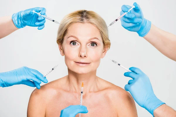 Hermosa y madura mujer mirando a la cámara con cosmetólogos sosteniendo jeringas — Stock Photo