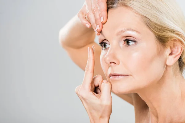 Selective focus of beautiful woman attaching contact lens isolated on grey — Stock Photo